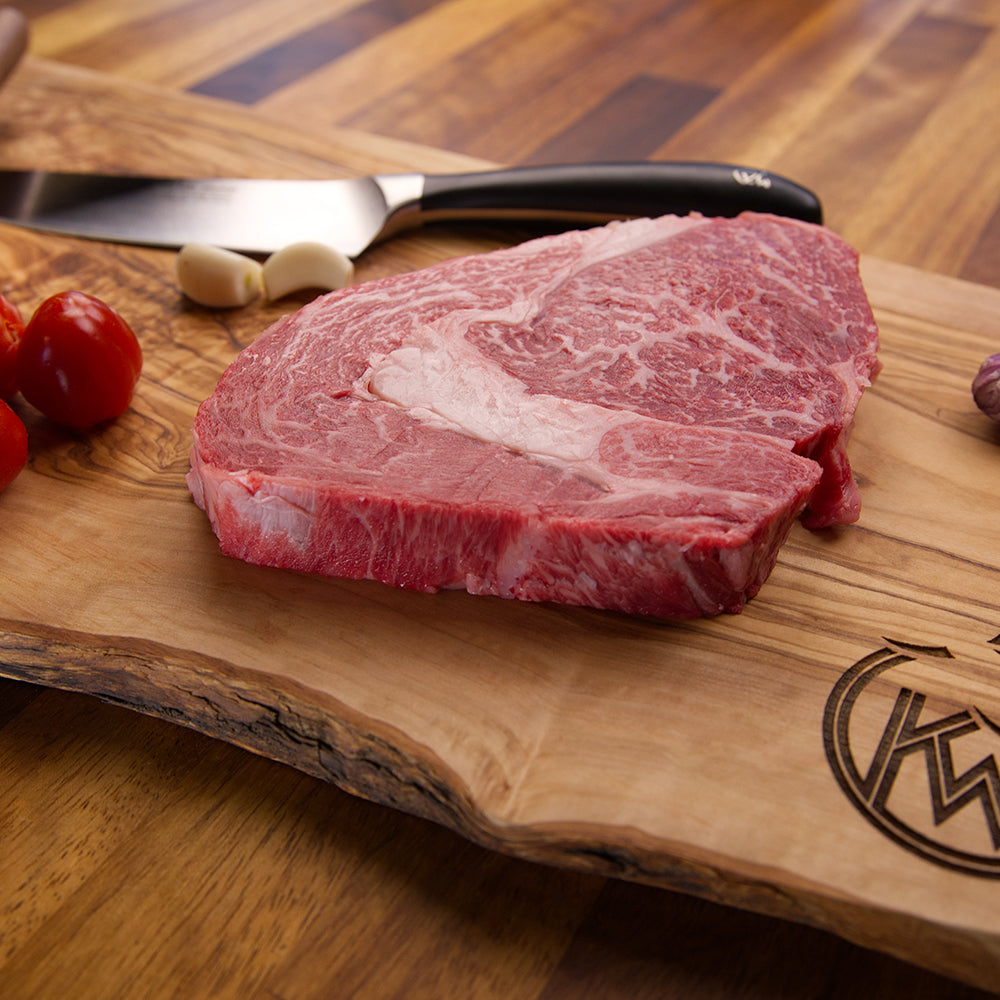 Close up of Kingsbury Wagyu Beef Ribeye on a chopping board with a knife, garlic and tomatoes